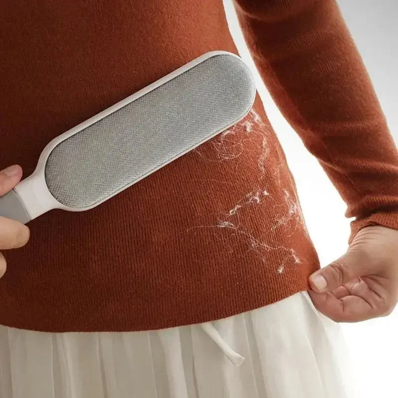 Hand using a pet hair remover brush on brown sweater to clean lint and pet fur.
