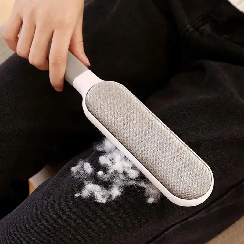 Hand using a pet hair remover brush to clean fur from black pants