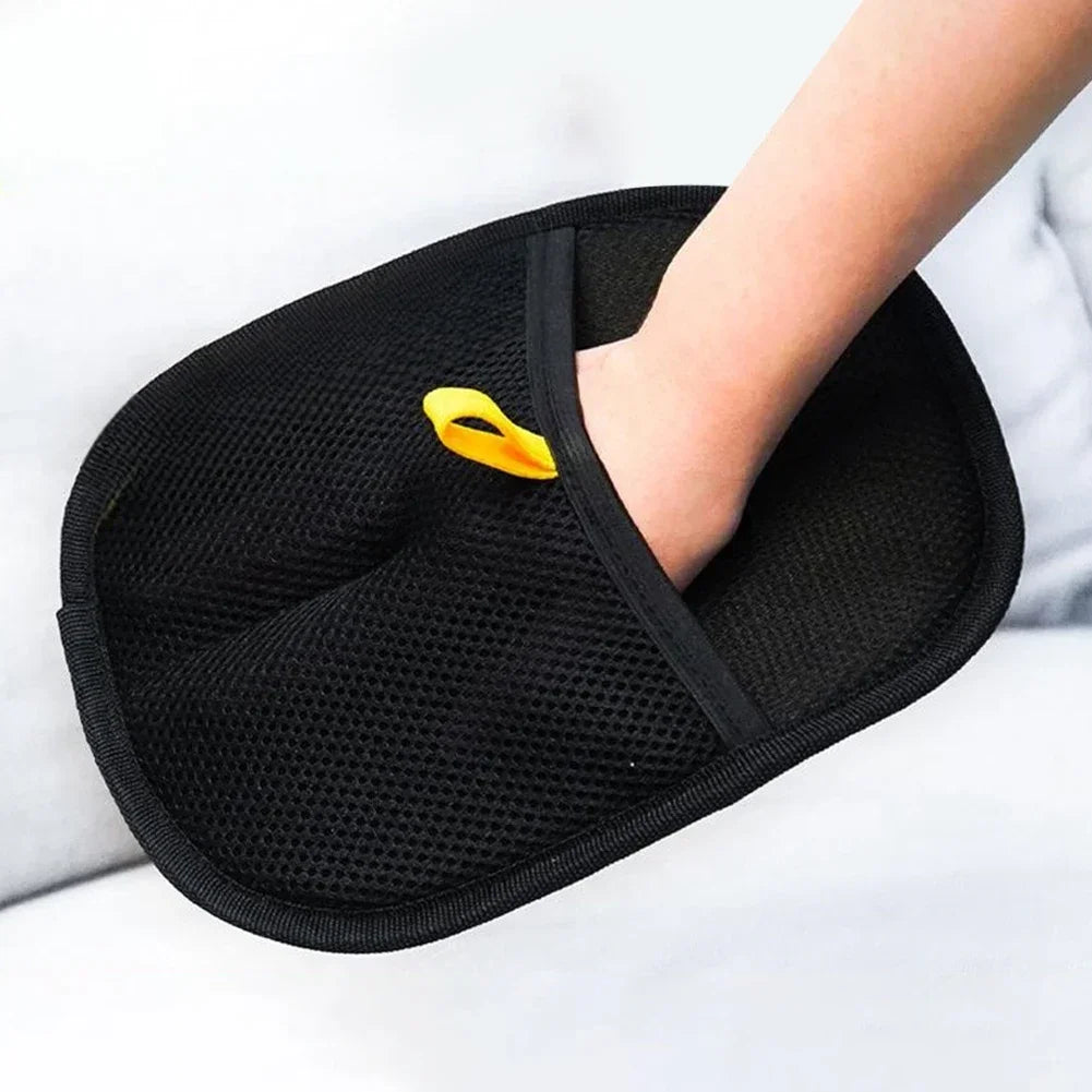 Hand wearing a black mesh pet grooming mitt with yellow hanging loop on light background