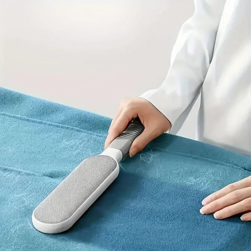 Person using a pet hair remover brush to clean fur from blue fabric surface